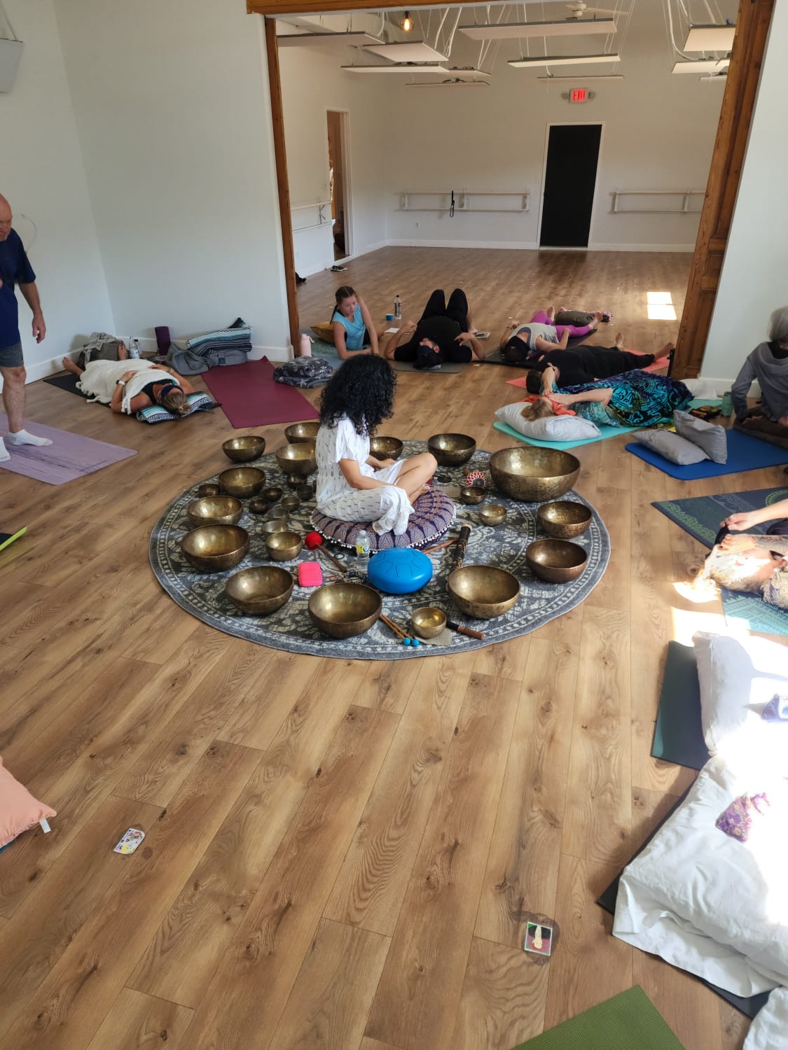 Participants settling onto mats and cushions around a circle of Himalayan singing bowls.